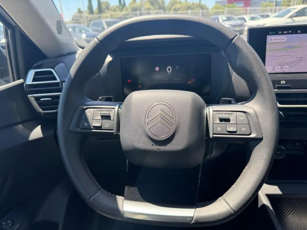 Vue rapprochée du volant cuir noir de la Citroën C4 hybride 2025 avec commandes intégrées et tableau de bord numérique.