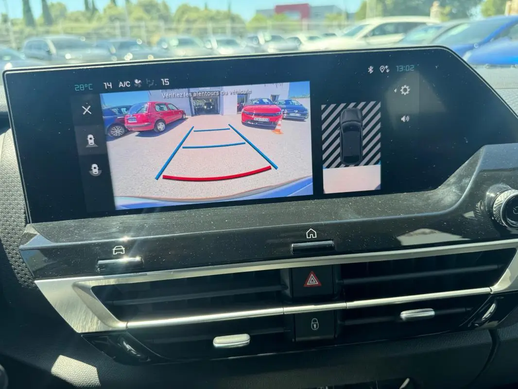 Écran intérieur montrant la caméra de recul avec vue arrière sur un parking ensoleillé.