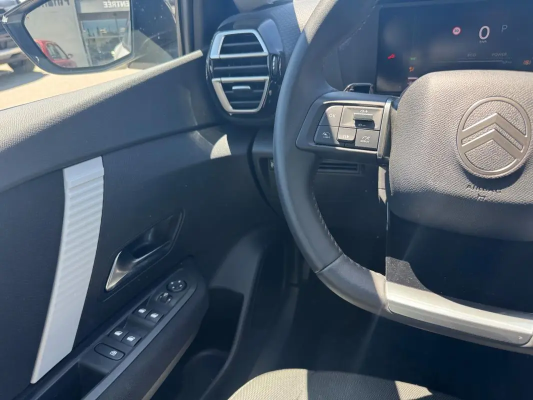 Vue intérieure côté conducteur du Citroën C4 hybride blanc 2025, volant cuir et commandes au volant visibles.