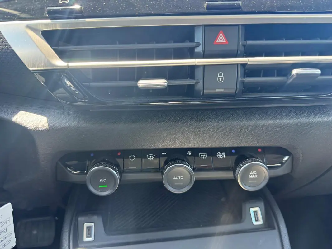 Gros plan sur la console centrale de la Citroën C4 hybride blanche, montrant les commandes de climatisation automatique et la prise USB.