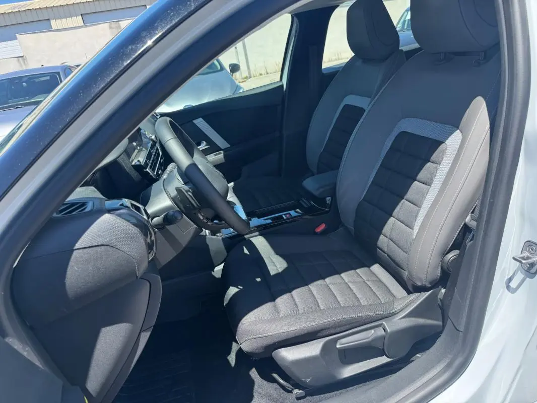 Vue intérieure côté conducteur de la Citroën C4 hybride blanche 2025, sièges tissu gris et volant cuir.