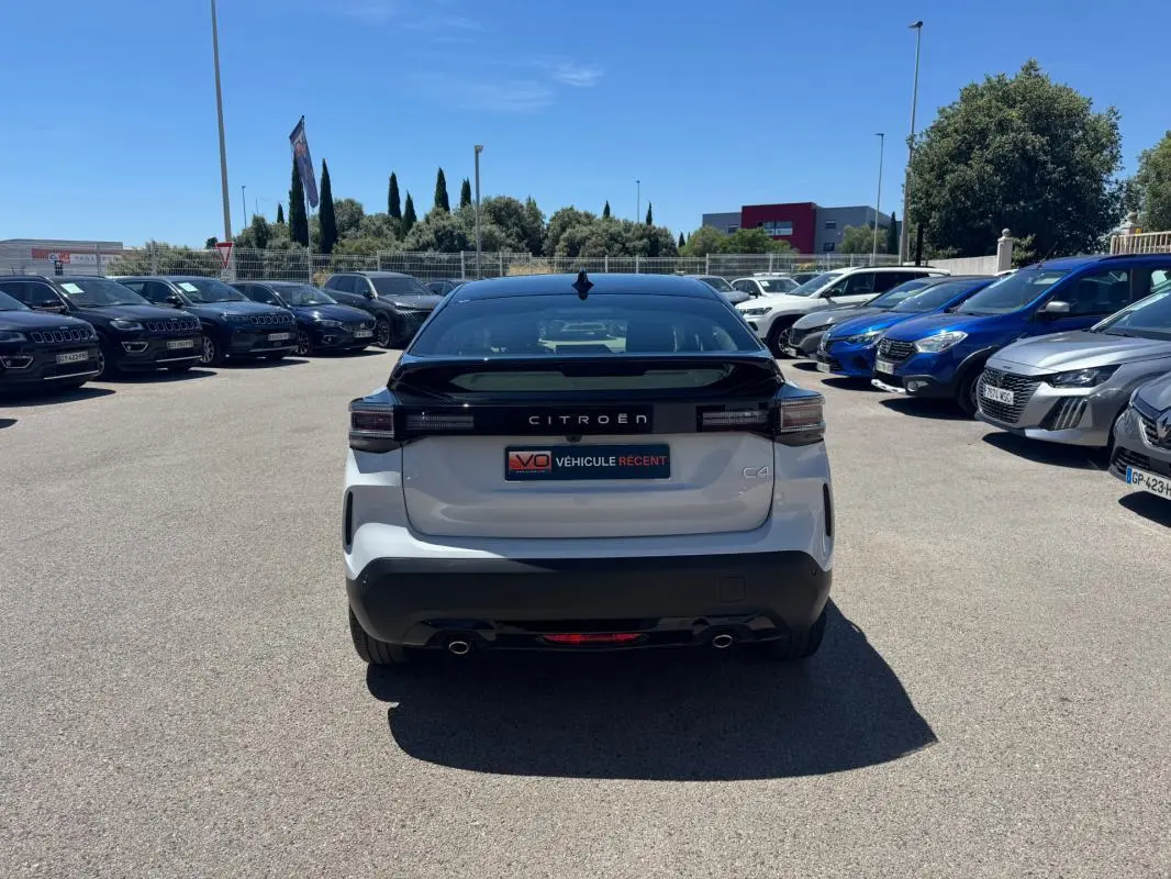 Vue arrière d'une Citroën C4 hybride blanche 2025 avec toit noir, feux arrière LED et double sortie d'échappement.