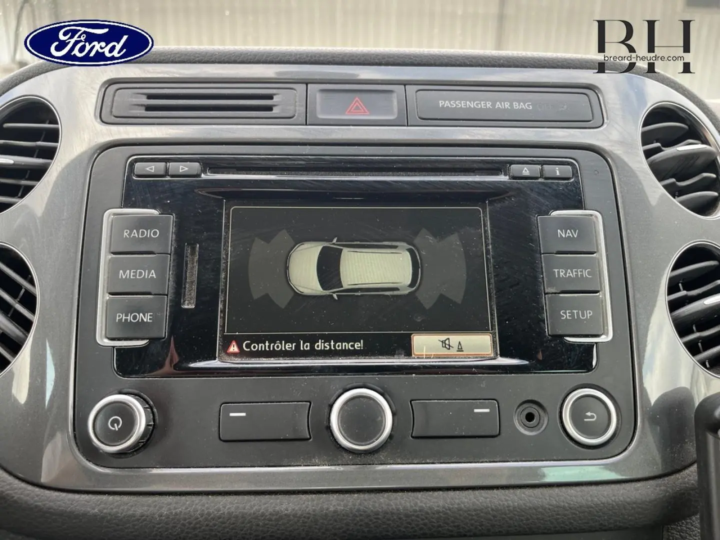 Tableau de bord avec écran tactile affichant l'aide au stationnement d'un Volkswagen Tiguan gris poivre, vue de face rapprochée.