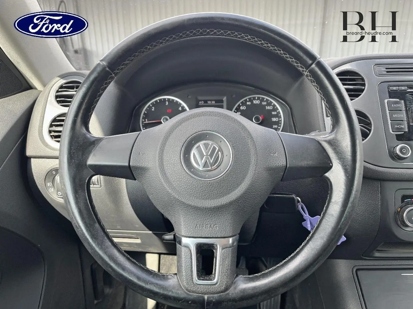 Vue rapprochée du volant noir avec logo Volkswagen au centre, tableau de bord et commandes visibles en arrière-plan.