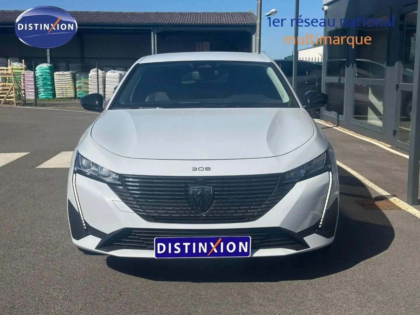 Vue avant d'une Peugeot 308 SW blanche Okénite avec calandre noire et feux LED verticaux allumés.