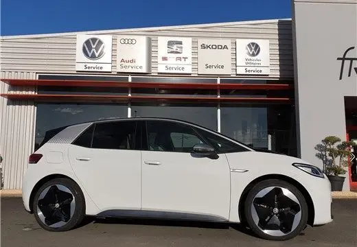 Profil droit d'une Volkswagen ID.3 blanc glacier garée devant un concessionnaire avec logos VW, Audi, Seat et Skoda.