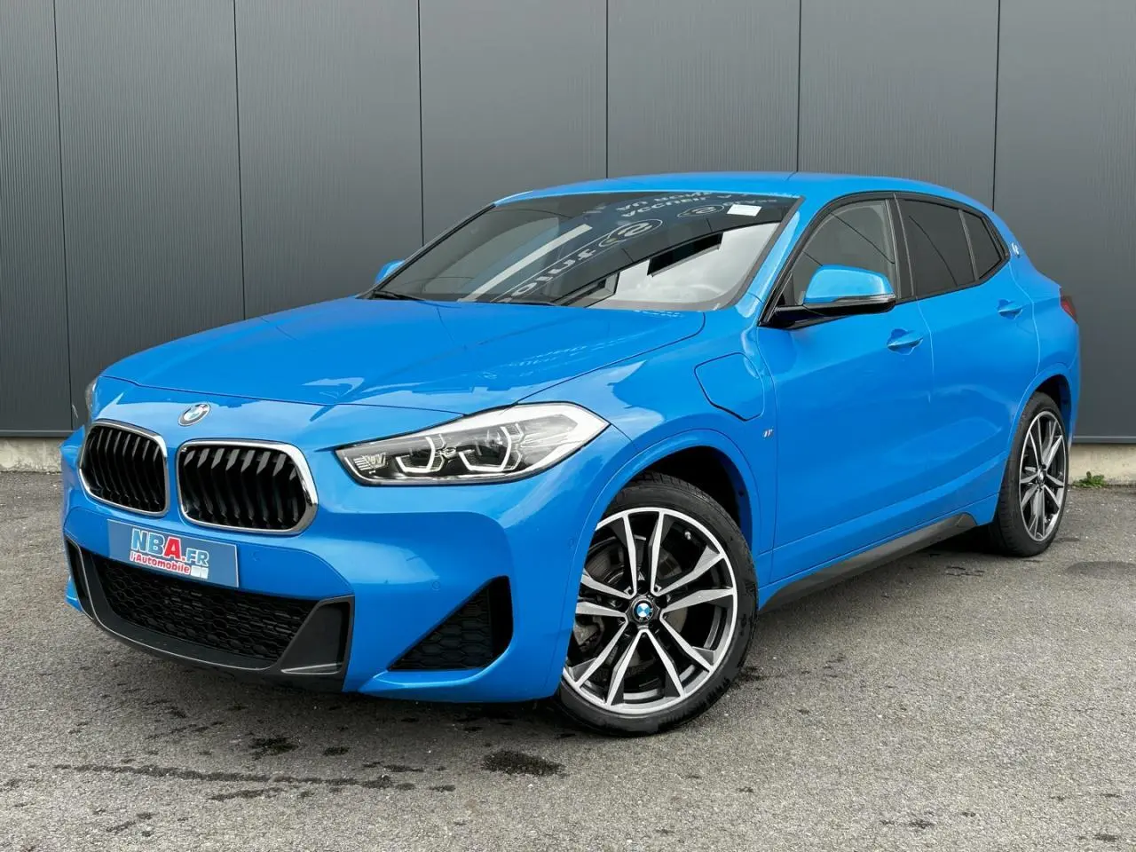 BMW X2 xDrive 25e bleu Misano en 3/4 avant droit, avec jantes alliage bicolores et calandre M Sport visible.