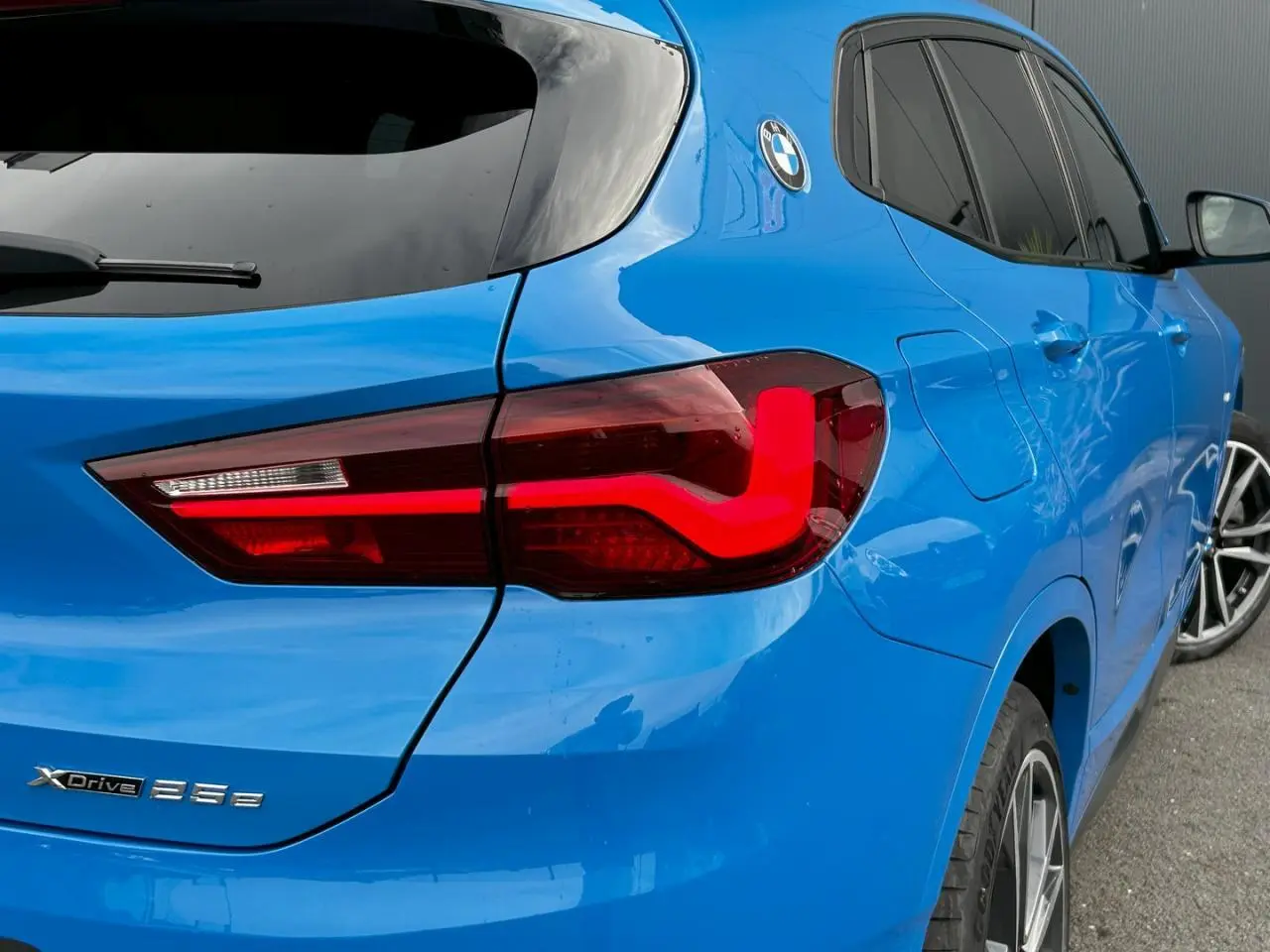 Vue 3/4 arrière droite d'une BMW X2 F39 xDrive 25e bleu Misano avec feux arrière LED et jantes alliage bicolores.