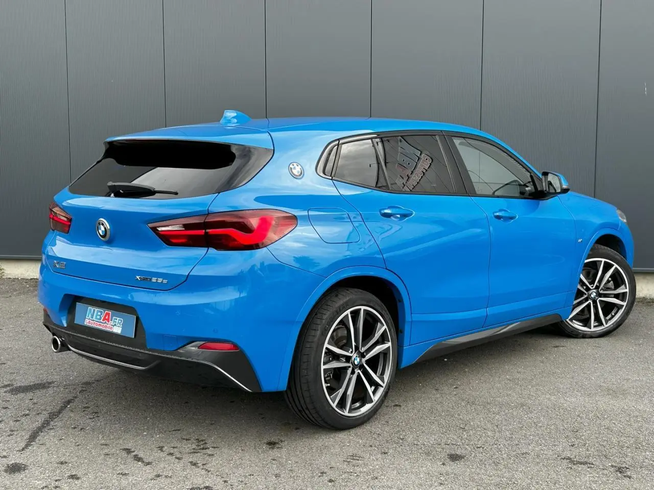 BMW X2 F39 xDrive 25e bleu Misano vue 3/4 arrière côté droit avec jantes alliage bicolores et vitres teintées