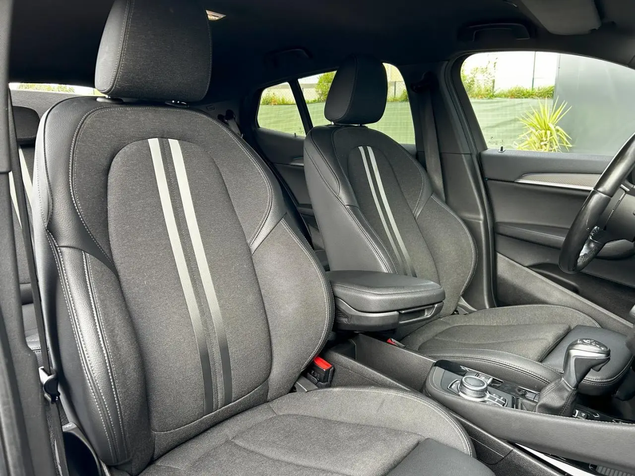 Intérieur avant de la BMW X2 F39 2021, sièges noirs avec bandes grises et accoudoir central visible côté droit.