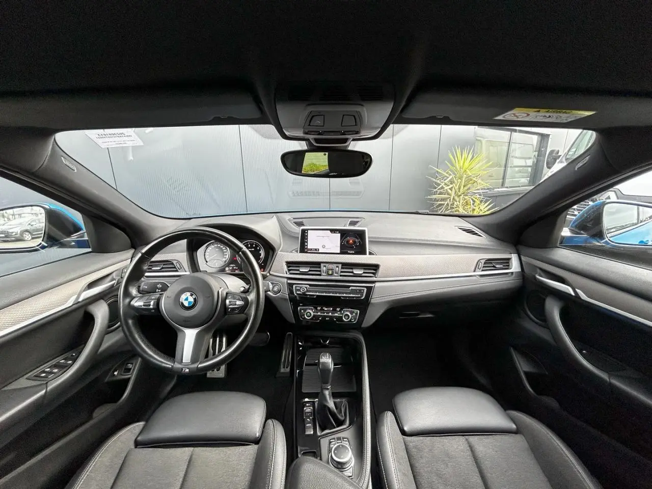 Vue intérieure avant du BMW X2 F39 2021, tableau de bord noir avec volant M cuir et écran GPS central.