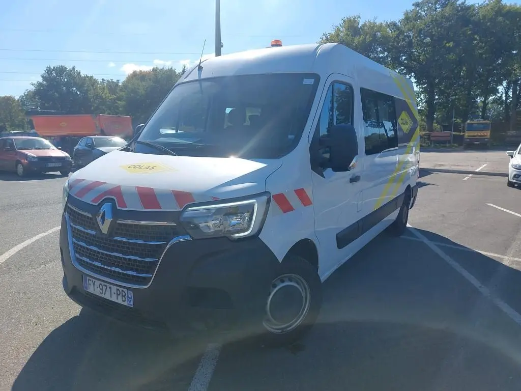 Renault Master blanc en 3/4 avant droit avec marquages rouges et jaunes et gyrophare sur le toit.
