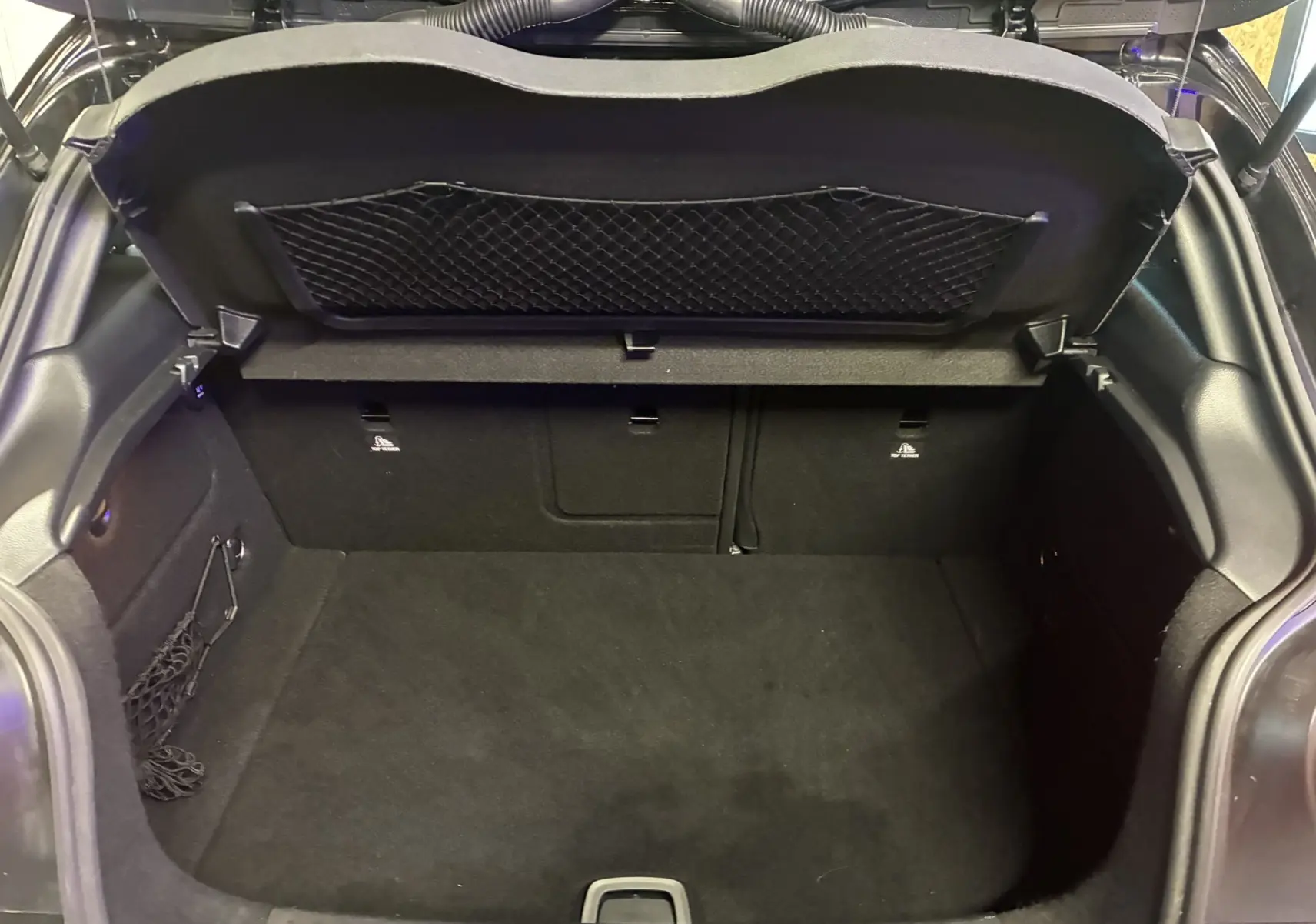 Coffre ouvert vu de l'arrière d'une Mercedes Classe A 180 CDI Sensation noire, intérieur de coffre noir et filet de rangement.