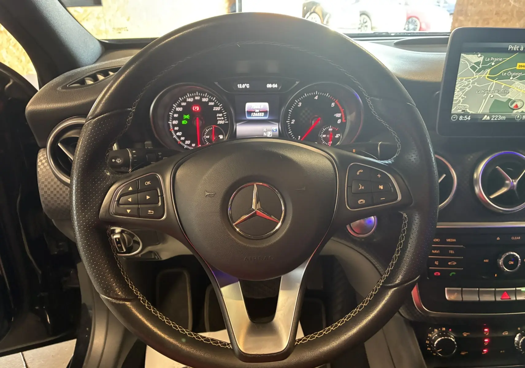 Vue rapprochée du volant noir en cuir perforé d'une Mercedes Classe A 180 CDI 2018 avec tableau de bord et écran GPS visibles.