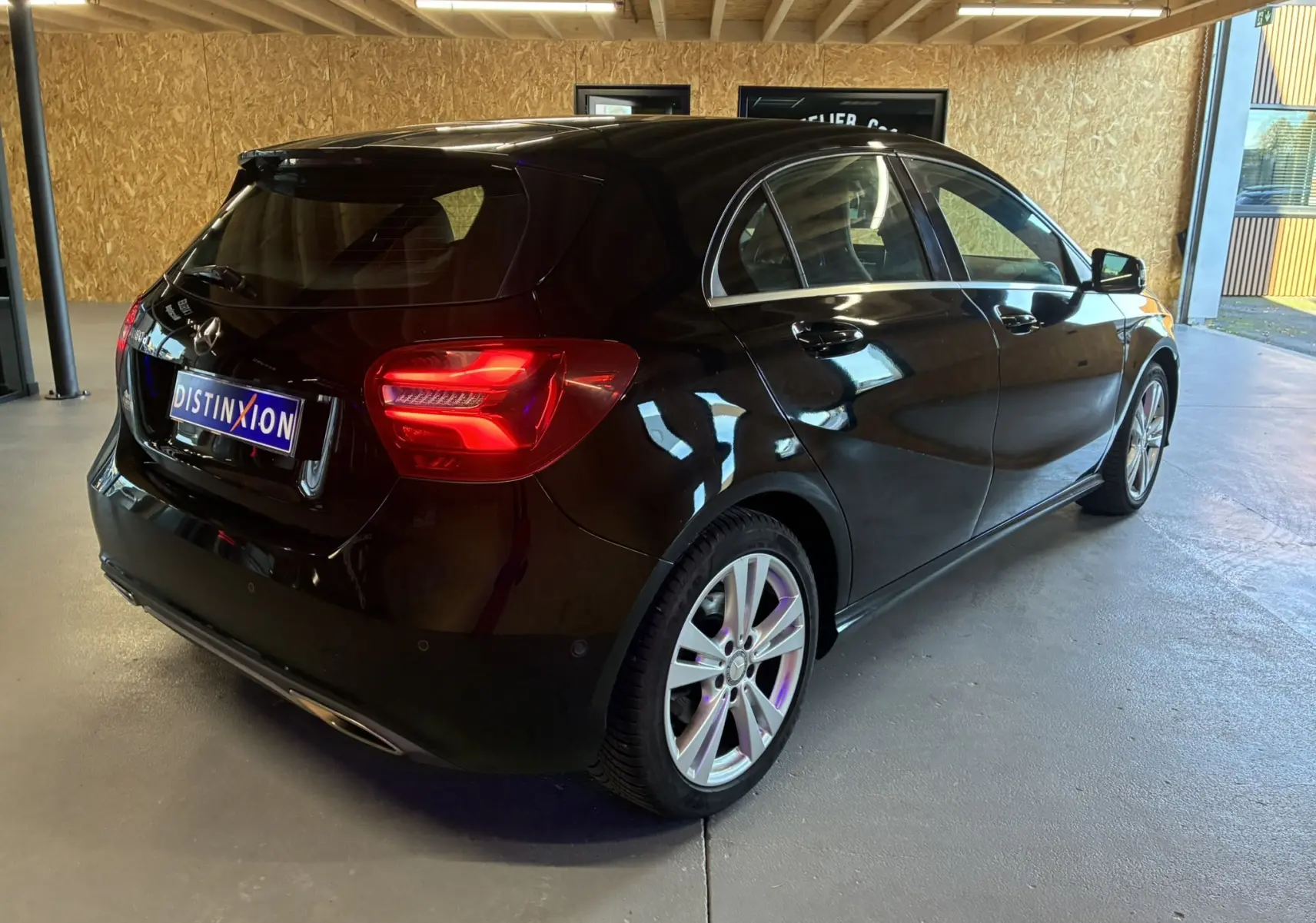 Mercedes Classe A 180 CDI noir vue 3/4 arrière droit en intérieur, feux arrière allumés et jantes alliage visibles