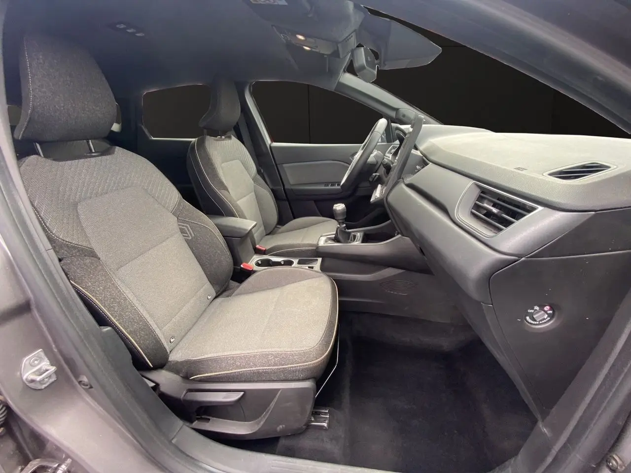 Vue intérieure côté conducteur du Renault Captur 2025 avec sièges tissu gris et tableau de bord noir.
