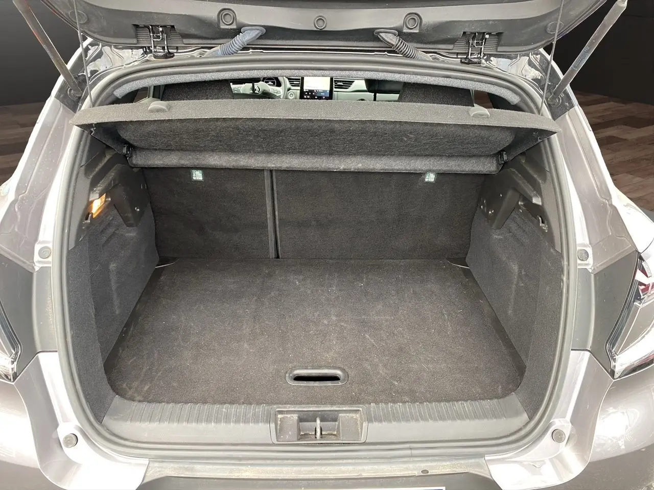 Coffre ouvert vu de l'arrière d'un Renault Captur gris Cassiopée avec intérieur noir et tablette cache-bagages.