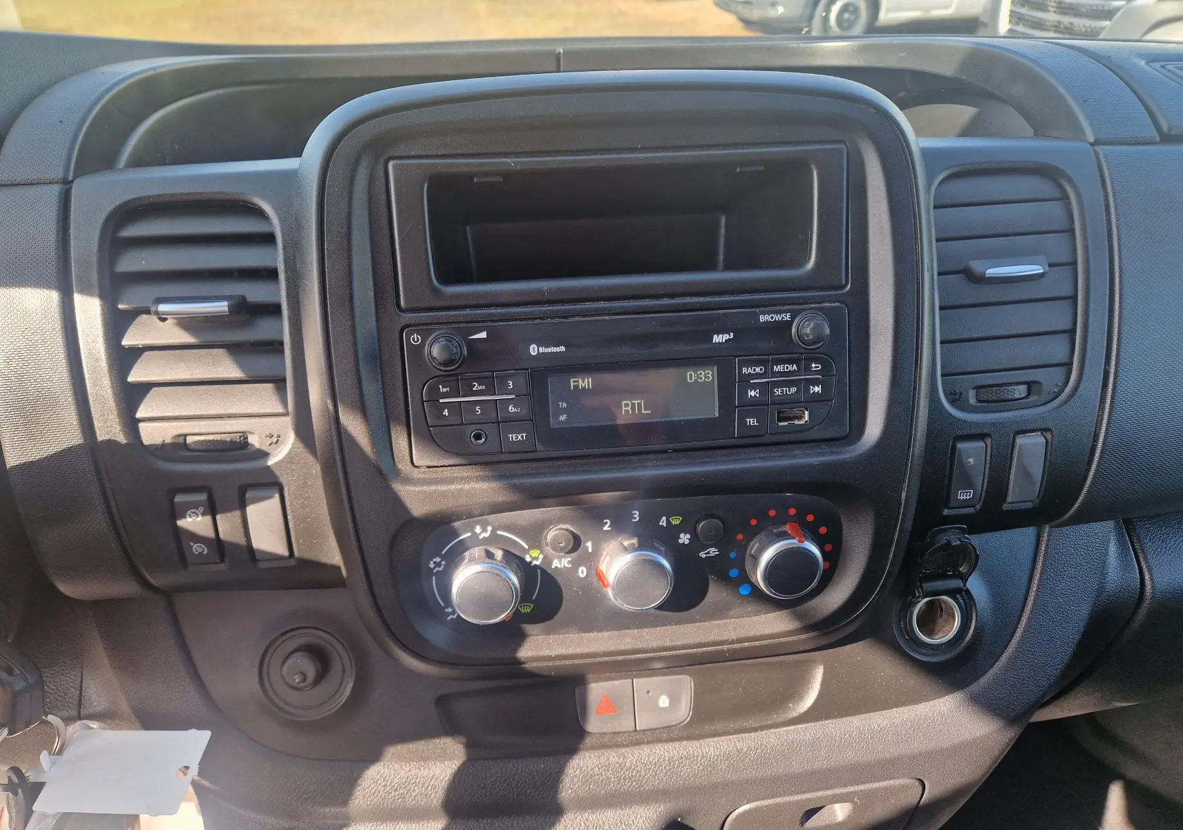 Vue rapprochée du tableau de bord noir du Renault Trafic Fourgon 2021 avec commandes climatisation et radio affichant RTL.
