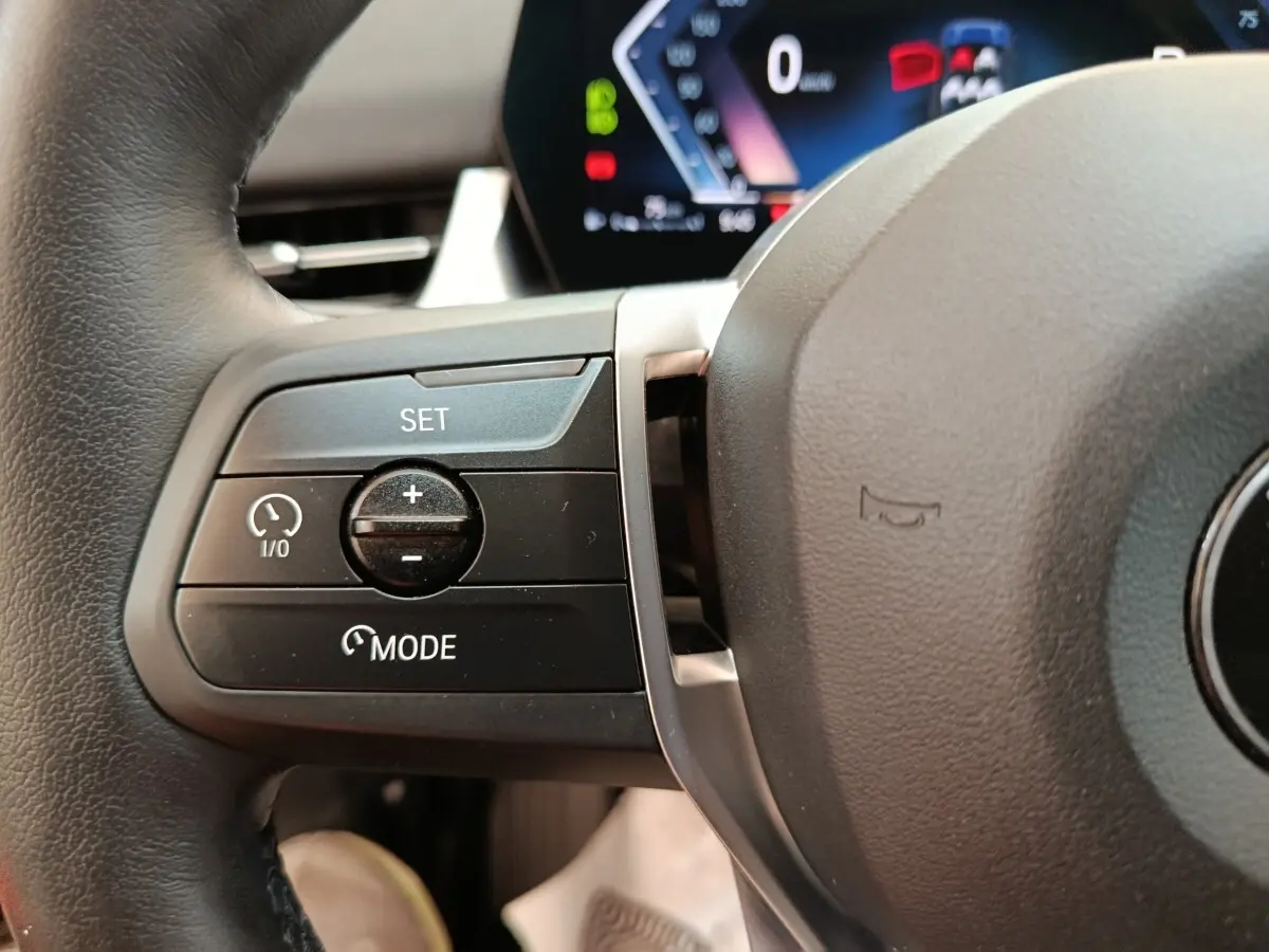 Gros plan sur le côté gauche du volant cuir noir de la BMW X1 2023 avec commandes de régulateur de vitesse.