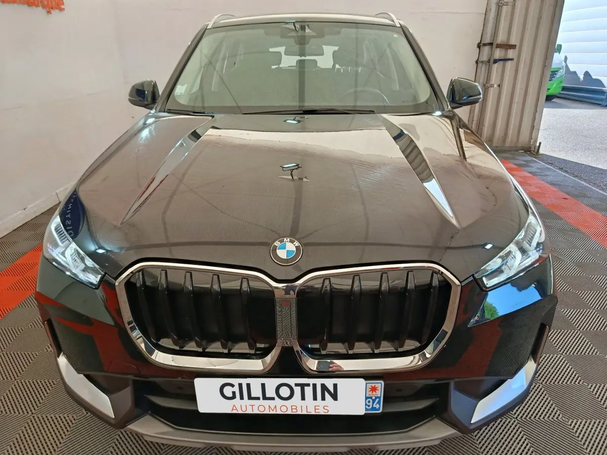 Vue avant d’un BMW X1 noir 2023 avec calandre imposante et phares LED dans un garage.