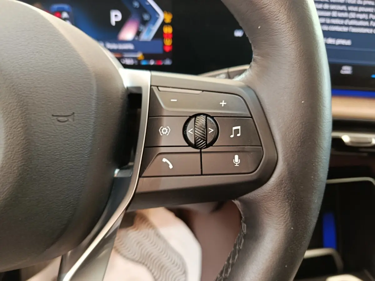 Gros plan sur le volant cuir noir de la BMW X1 2023, avec commandes multifonctions visibles côté droit.