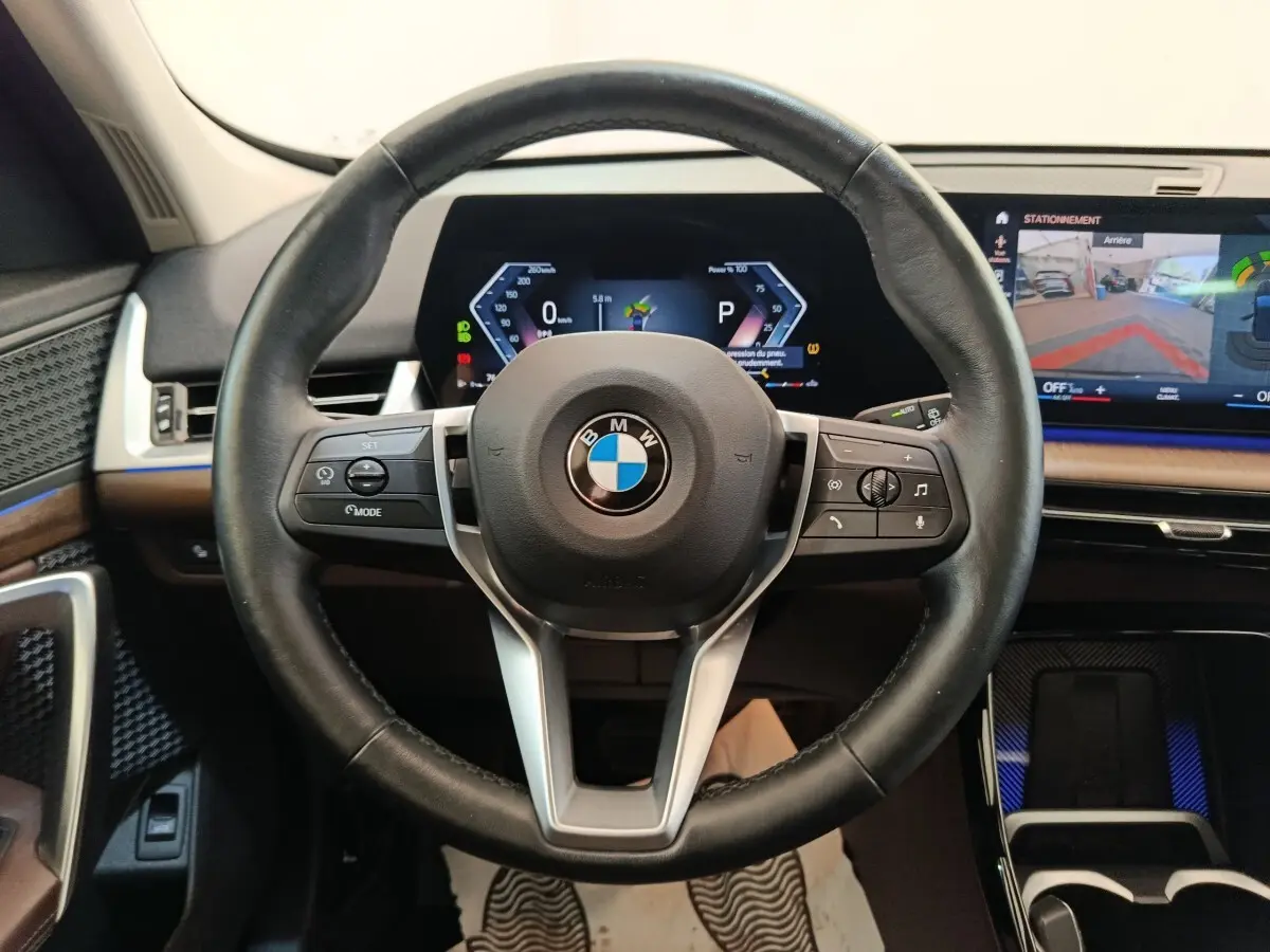Vue centrée sur le volant cuir noir multifonctions de la BMW X1 2023 avec tableau de bord digital et écran tactile.