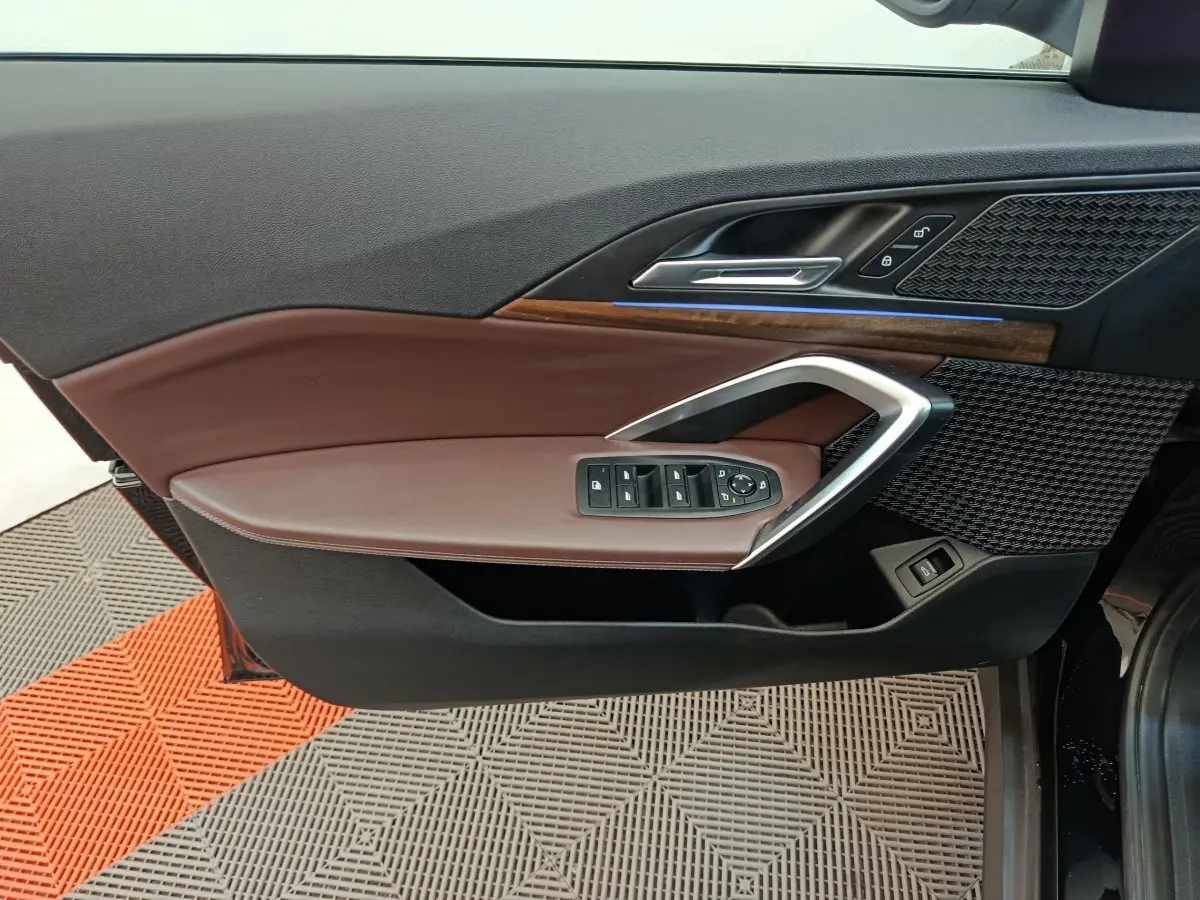 Vue intérieure du panneau de porte côté conducteur de la BMW X1 2023, avec garniture marron et inserts bois et métal.