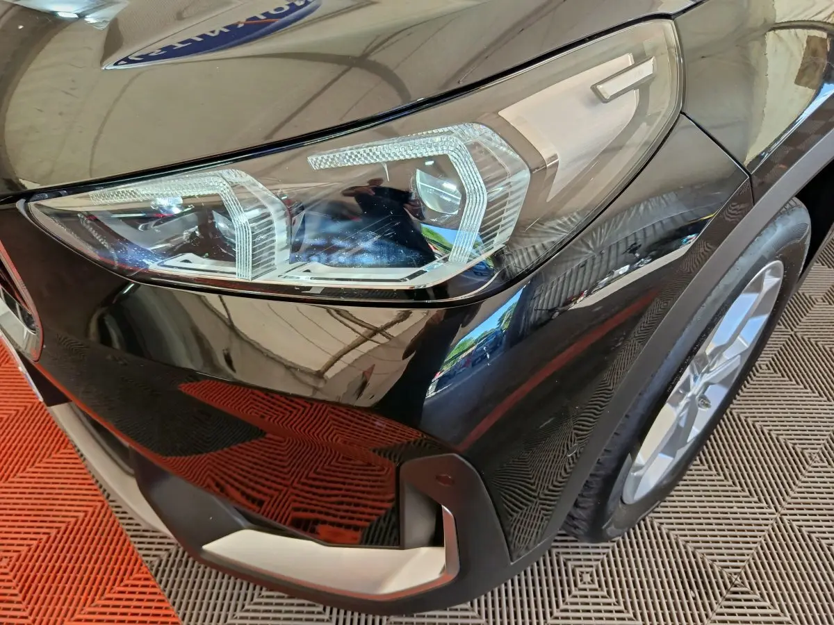 Gros plan sur le phare avant droit d’un BMW X1 noir 2023 avec jante alliage et pare-chocs argenté.