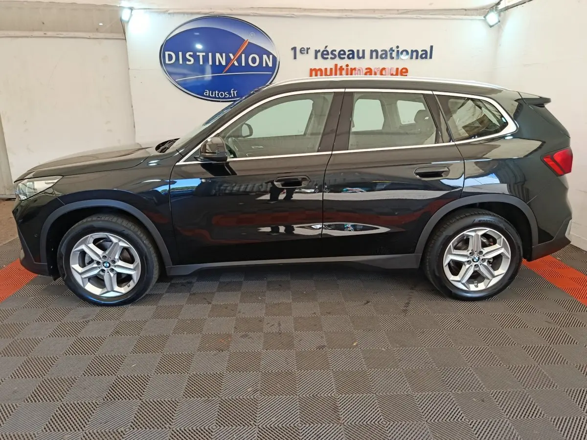 BMW X1 sDrive18i Business Design noir vue de profil côté gauche, avec jantes alliage et toit spoiler visible.
