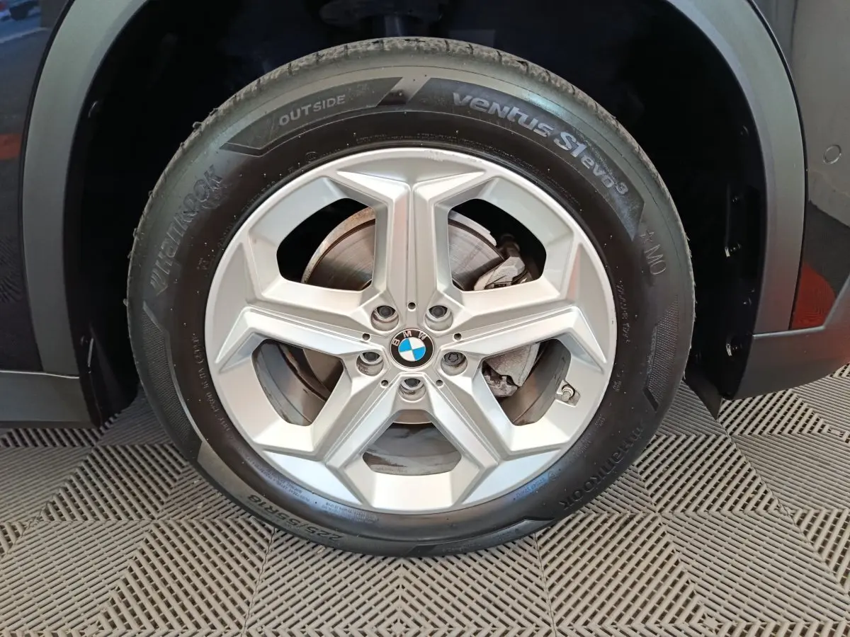Gros plan sur la roue avant droite de la BMW X1 noire, mettant en valeur la jante alliage à cinq branches.