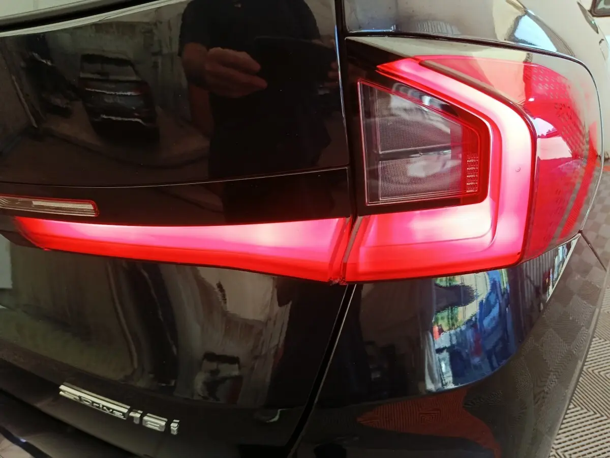 Gros plan sur le feu arrière droit rouge vif d’un BMW X1 noir sDrive18i, avec reflet de l’environnement sur la carrosserie.