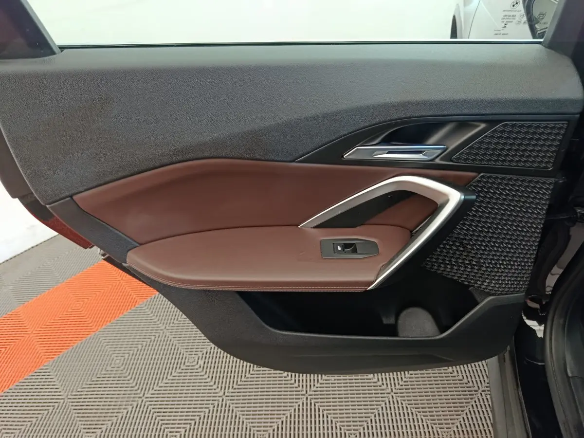 Gros plan sur la porte avant gauche intérieure du BMW X1 noir, avec garniture marron et insert argenté.