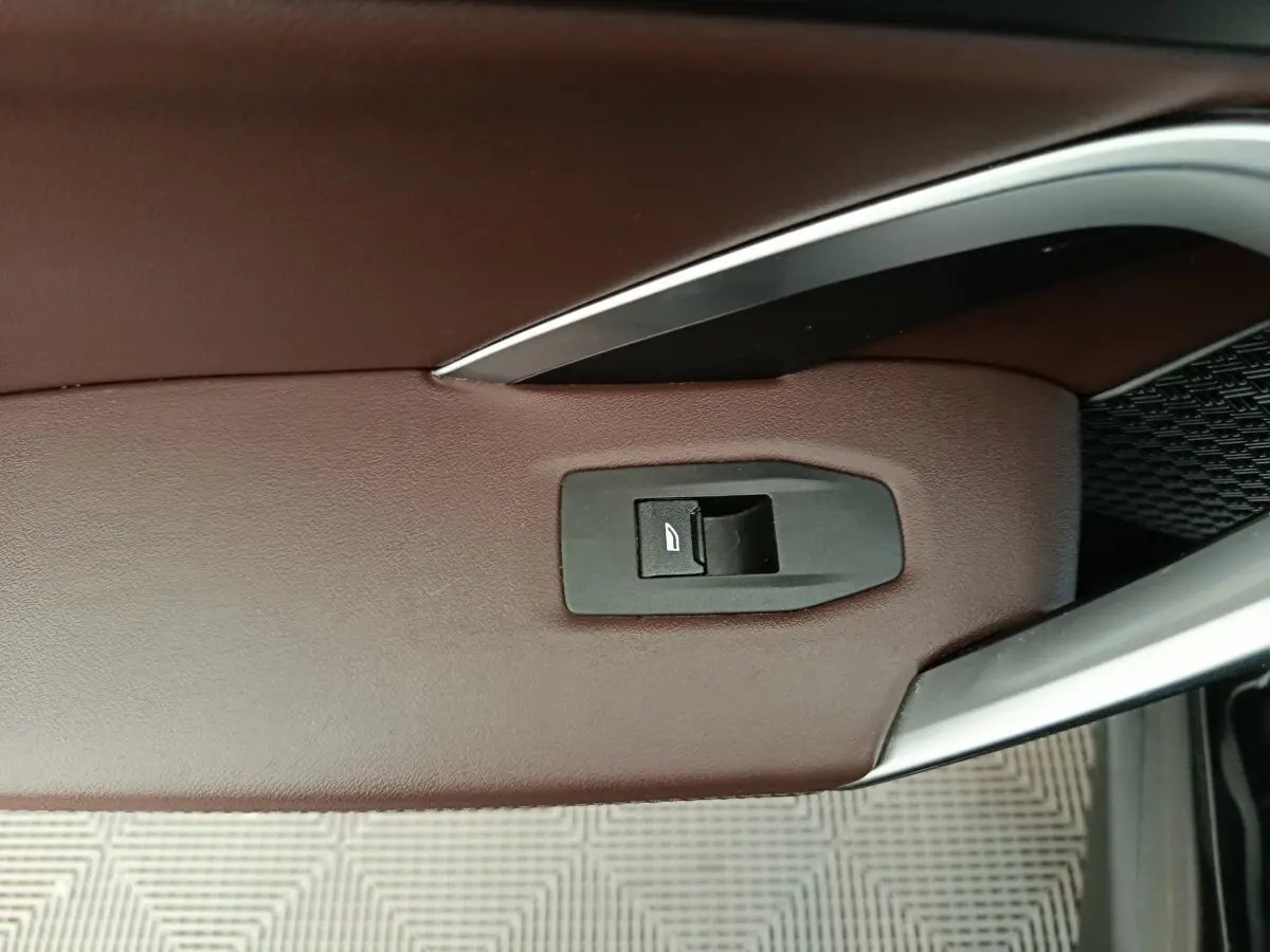 Détail de la commande de lève-vitre sur la porte côté conducteur en cuir marron du BMW X1 noir 2023.
