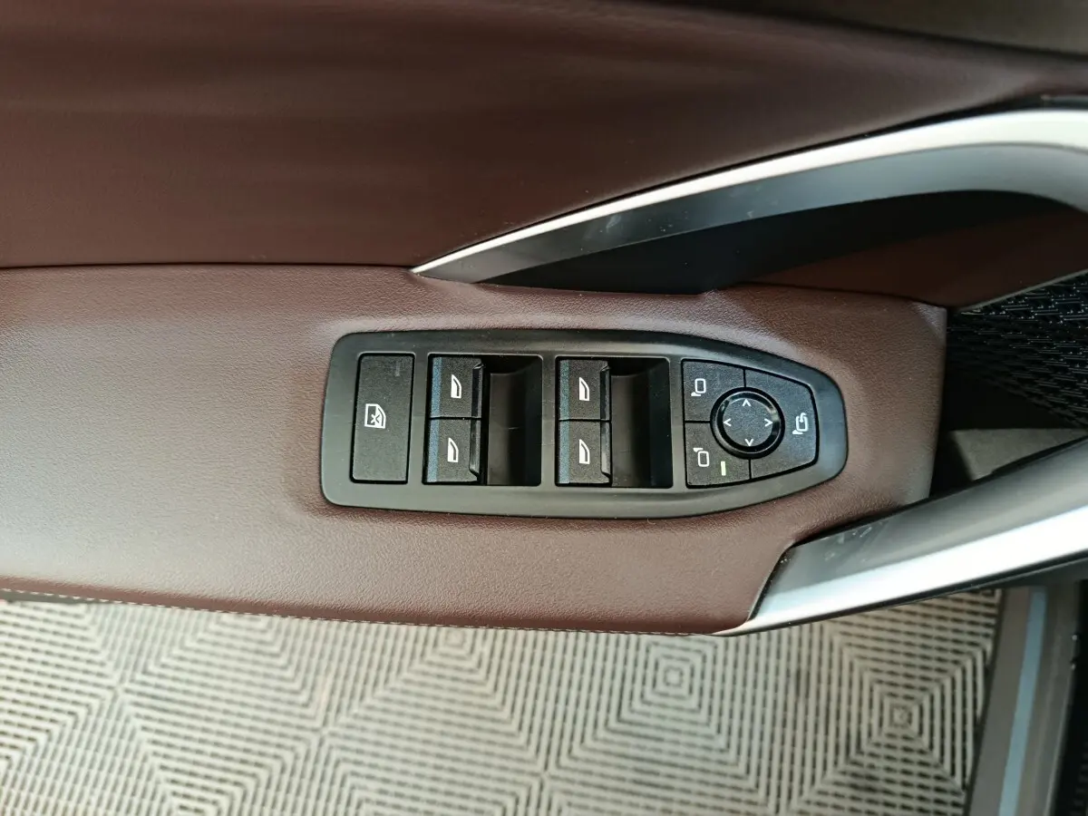 Vue rapprochée des commandes de lève-vitres et rétroviseurs sur la porte côté conducteur en cuir marron du BMW X1 noir 2023.