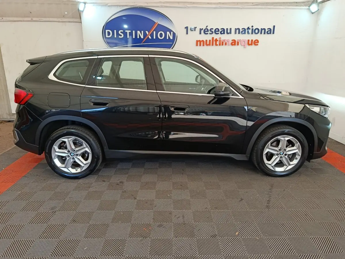 BMW X1 sDrive18i Business Design noir vue de profil côté gauche dans un showroom avec logo Distinxion en arrière-plan.