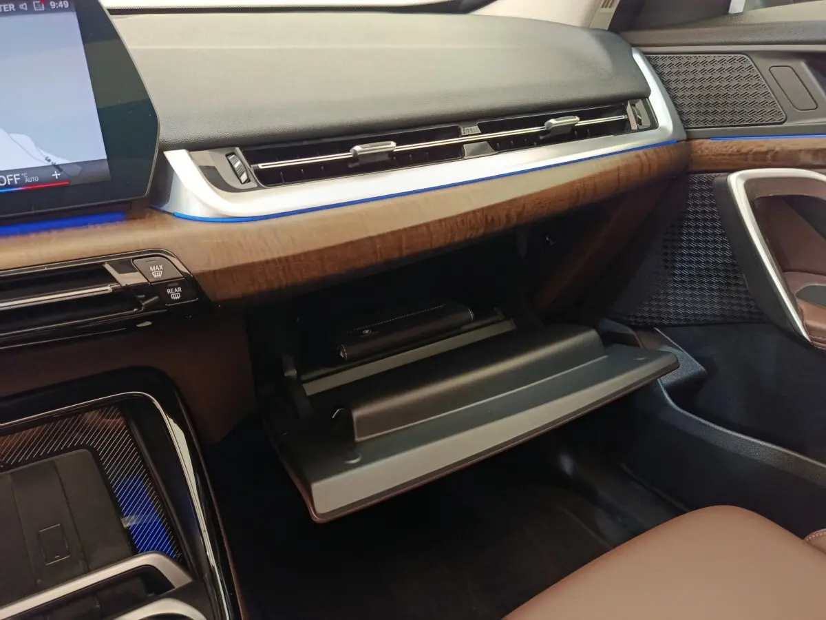 Intérieur BMW X1 2023 sDrive18i, vue côté passager sur boîte à gants ouverte et tableau de bord bois et noir.