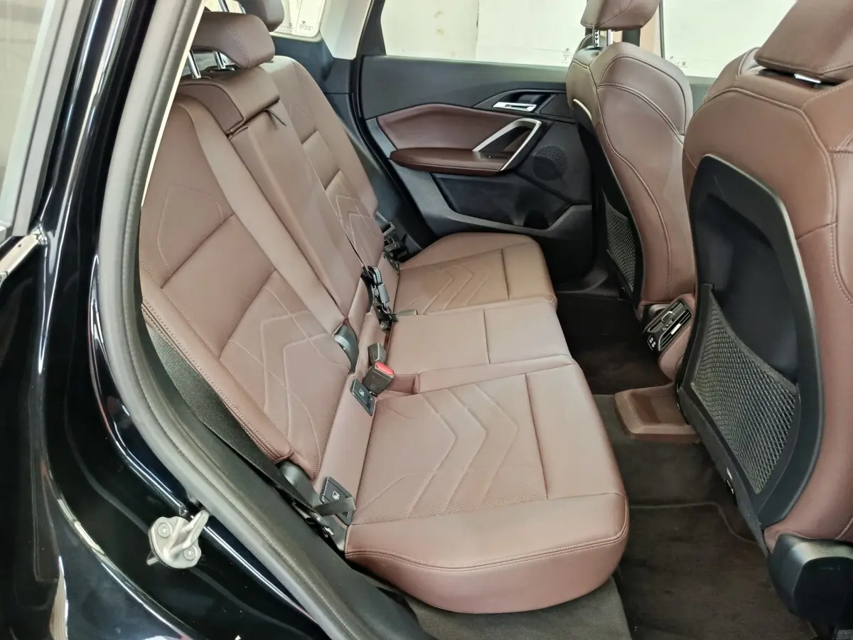 Vue intérieure côté gauche des sièges arrière en cuir marron d'une BMW X1 noire, avec banquette 3 places et rangements filet.