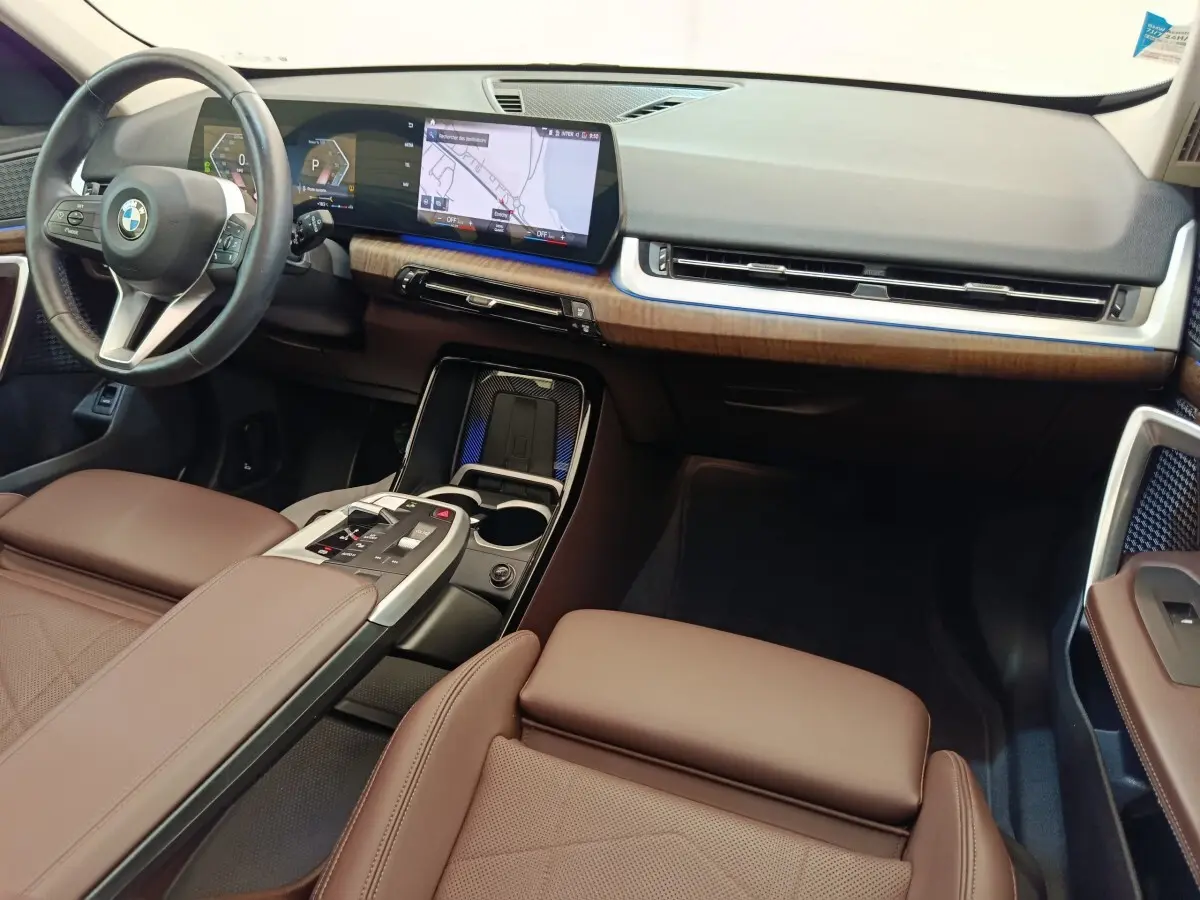Vue intérieure avant droite du BMW X1 2023 avec tableau de bord noir, inserts bois et sièges cuir marron.