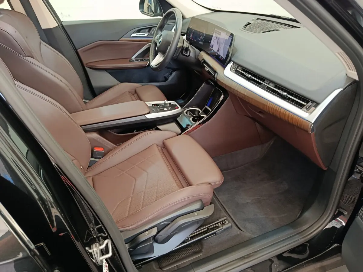 Vue intérieure côté conducteur de la BMW X1 2023 noire, sièges cuir marron et tableau de bord avec écran tactile.
