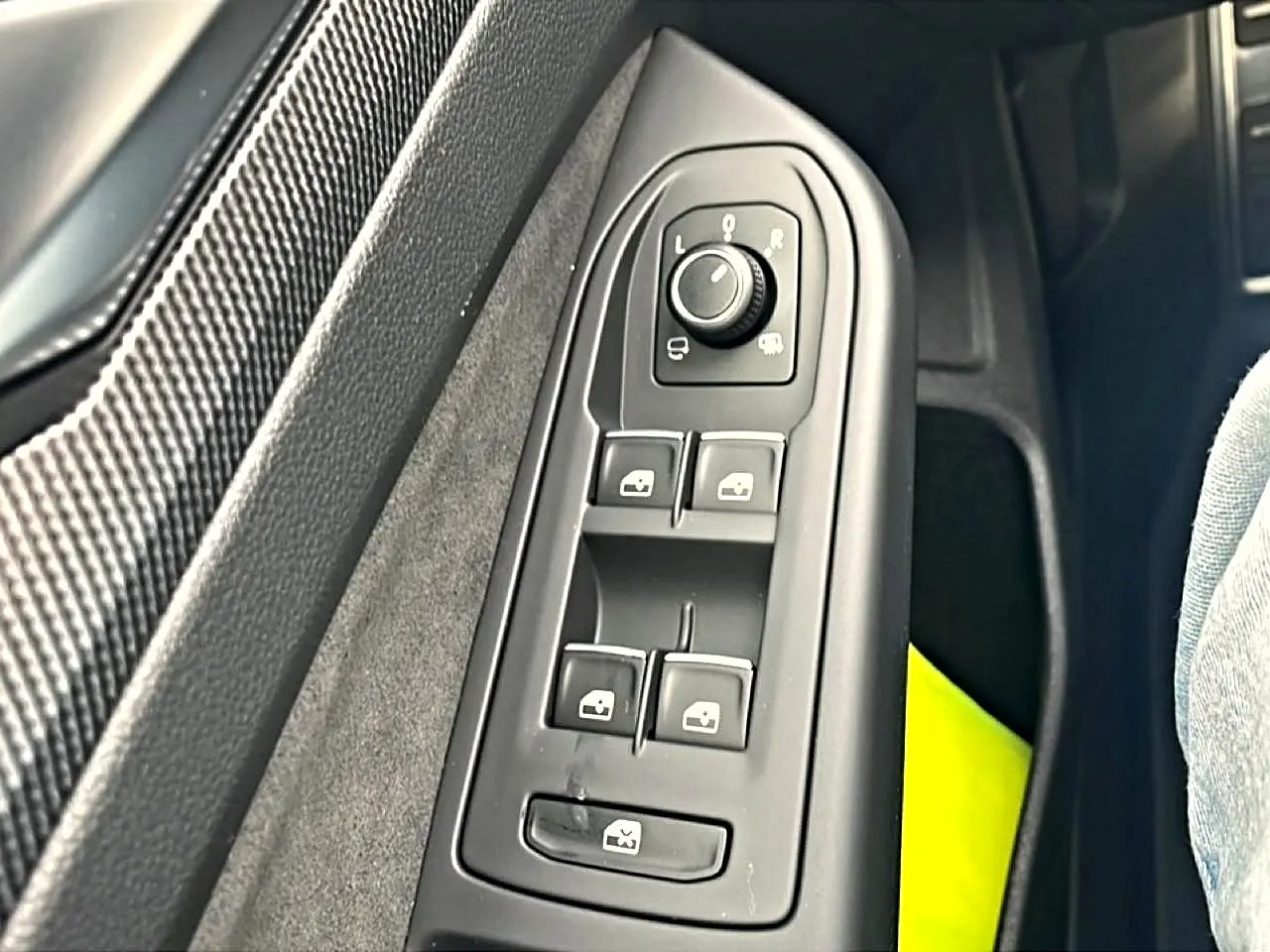 Gros plan sur les commandes de lève-vitres et rétroviseurs côté conducteur d’une Volkswagen Golf noire.