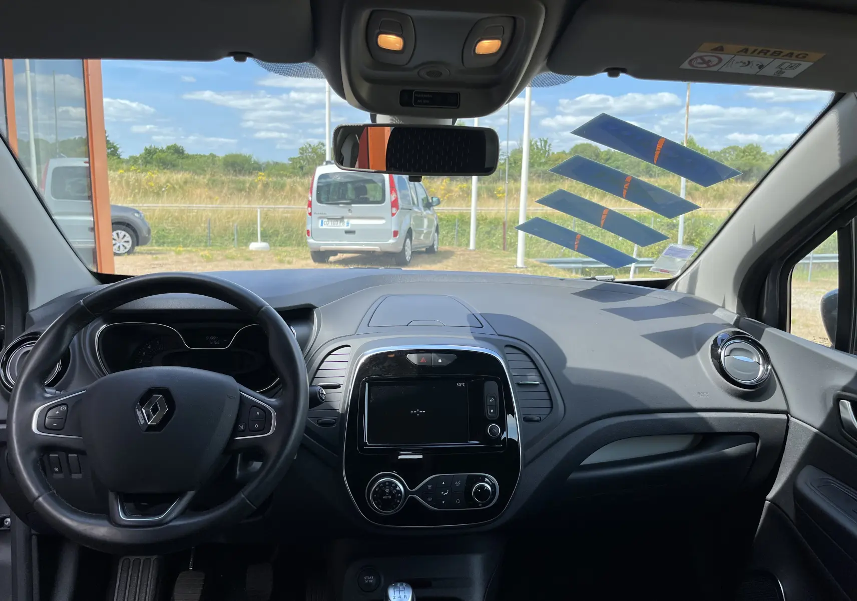 Vue intérieure frontale du tableau de bord noir du Renault Captur gris 2019 avec volant cuir et écran tactile central éteint.