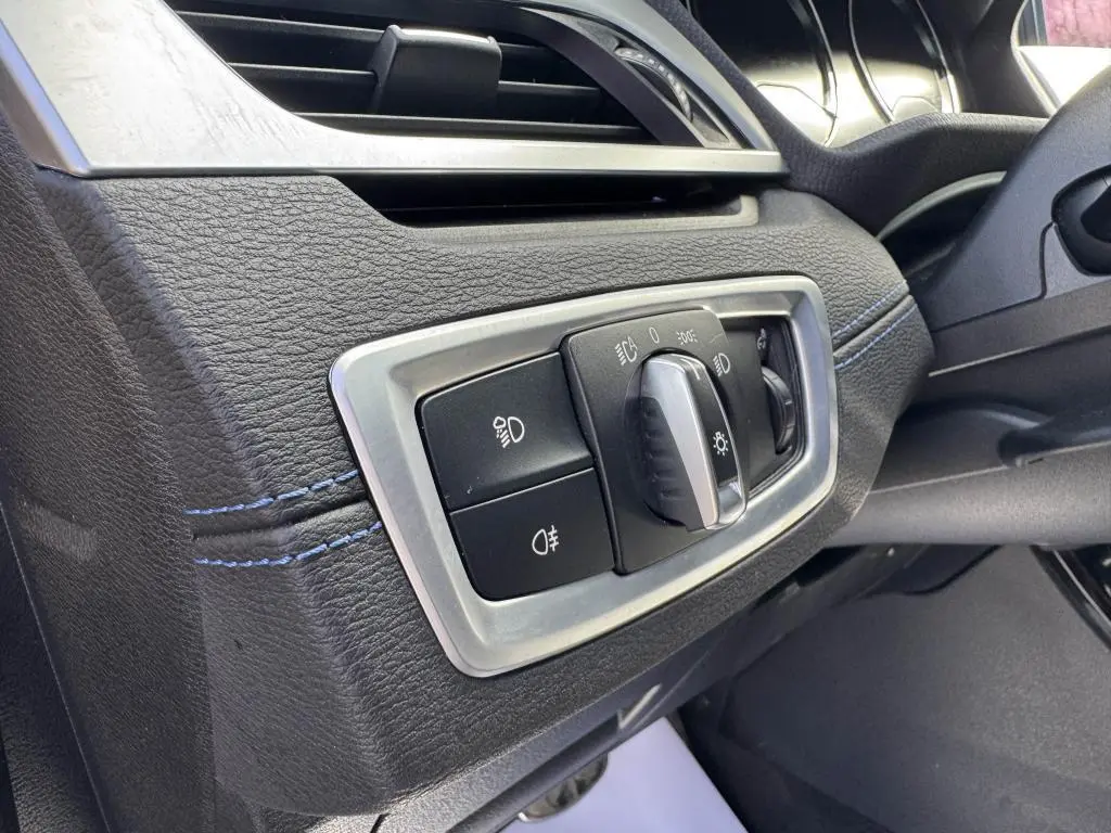 Gros plan sur le bouton de commande des phares à gauche du volant dans l’habitacle noir avec surpiqûres bleues du BMW X2 jaune M Sport 2021.