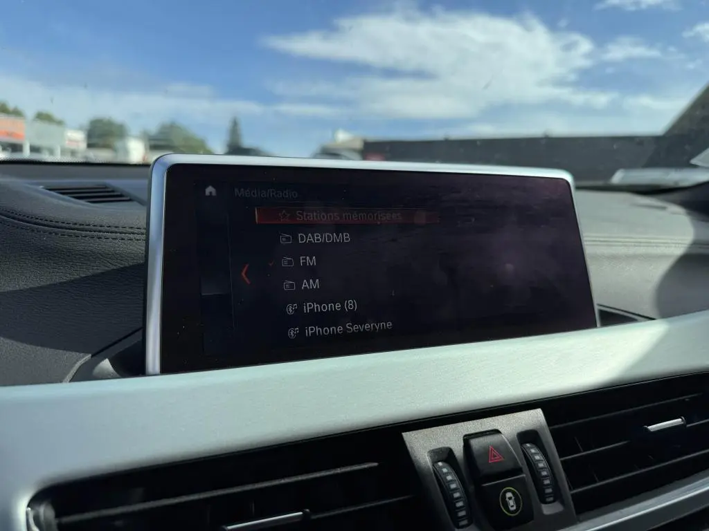 Écran multimédia central affichant les options radio dans l'habitacle d'une BMW X2 jaune vue de face intérieure.