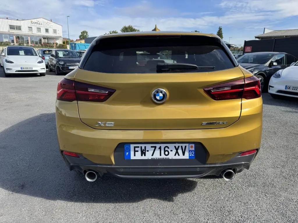Vue arrière d'un BMW X2 sDrive 18d jaune métallisé avec double sortie d'échappement et feux arrière LED.