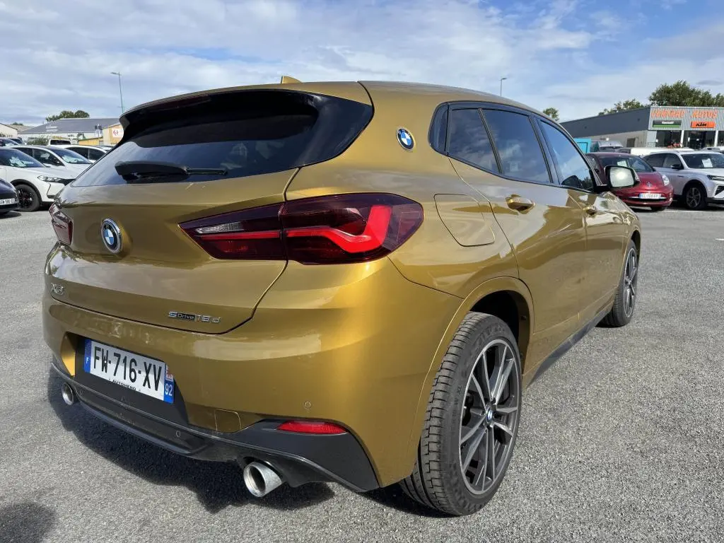 Vue 3/4 arrière droite d'un BMW X2 sDrive18d jaune métallisé avec jantes 19 pouces et double sortie d'échappement chromée.