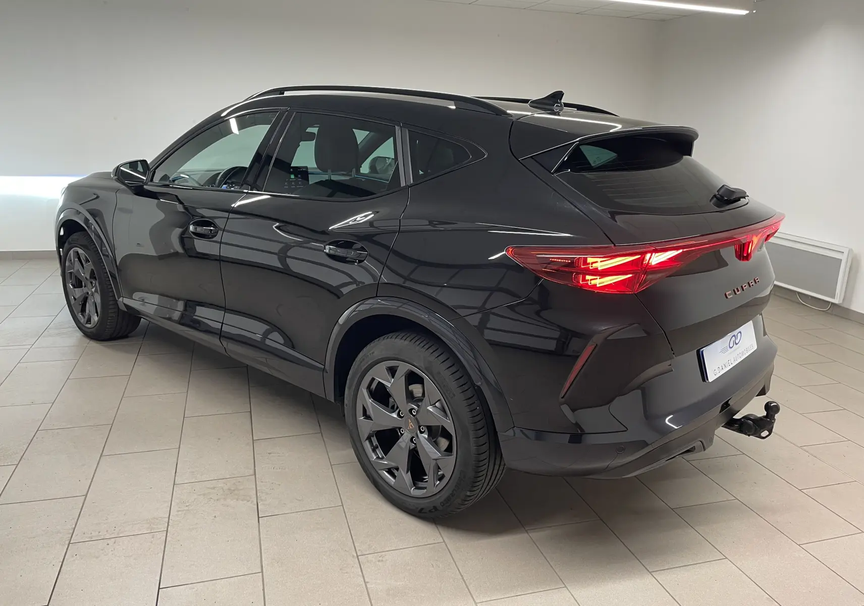 Vue 3/4 arrière droite du CUPRA Formentor noir minuit avec feux allumés et crochet d'attelage escamotable visible.