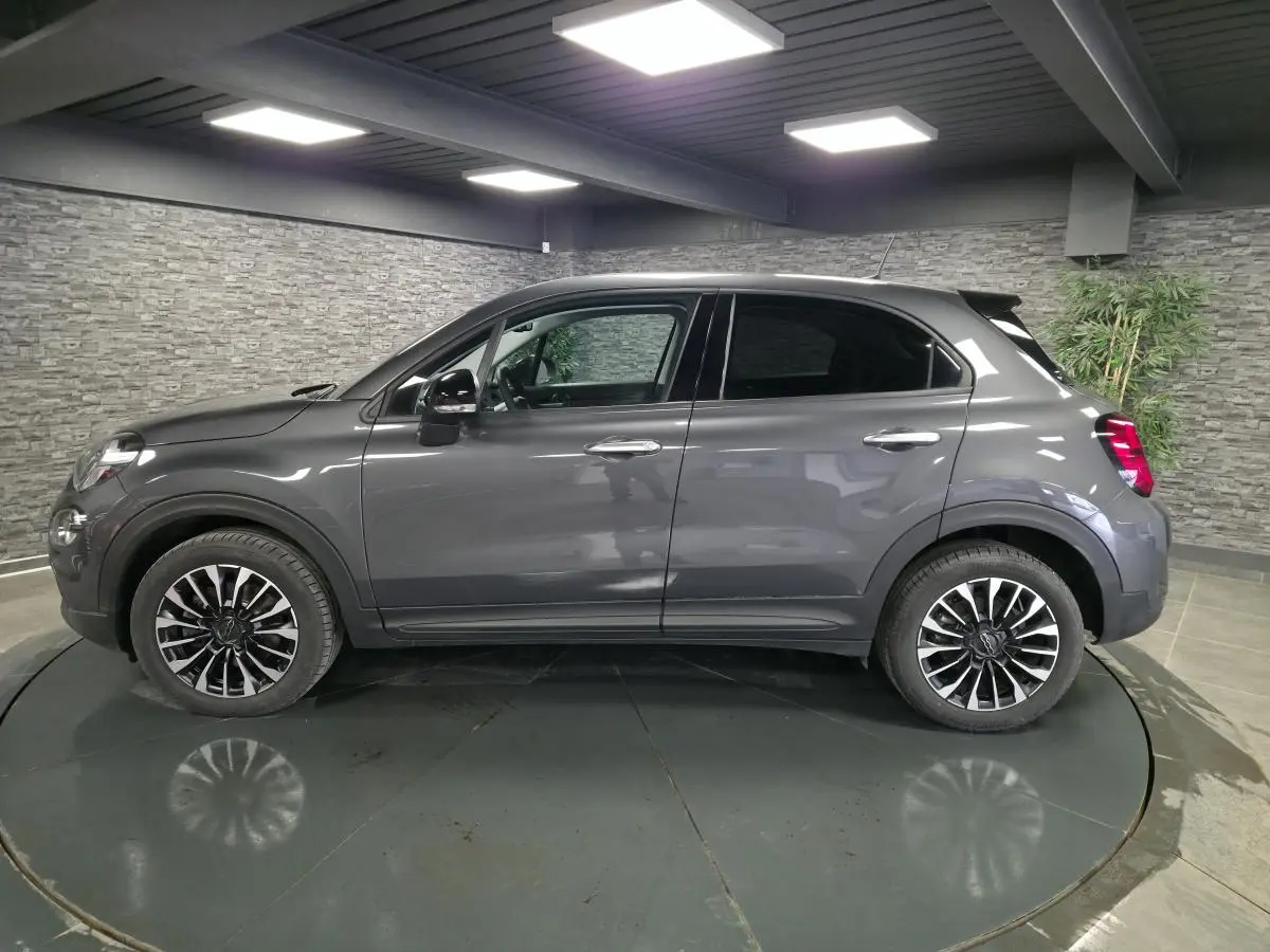 Profil droit d'un Fiat 500X gris avec jantes alliage 17 pouces et vitres surteintées dans un showroom.