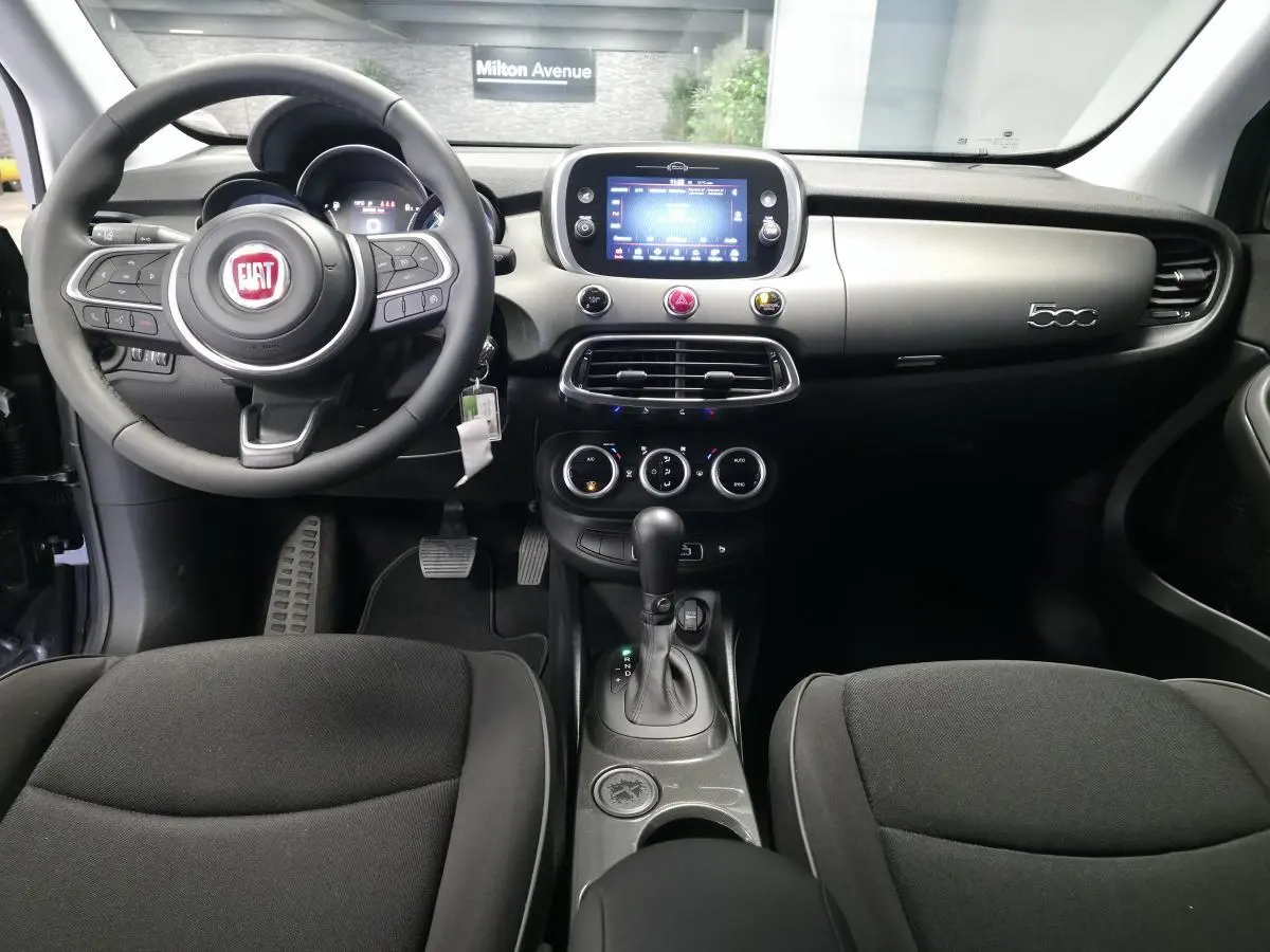Intérieur de la Fiat 500X 2024 en vue frontale, tableau de bord gris titane avec écran tactile et volant Soft-Touch noir.
