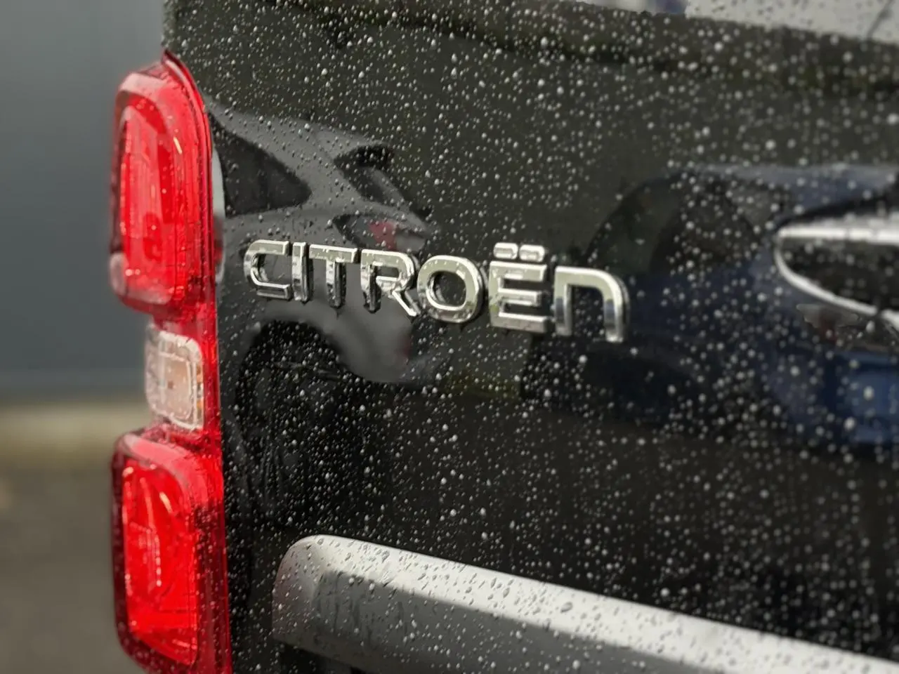 Gros plan sur l'arrière gauche noir perla d'un Citroën Jumpy avec logo et feux rouges sous la pluie.