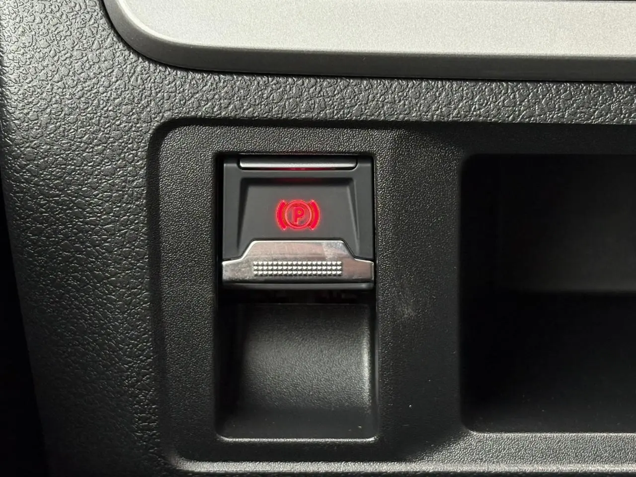 Gros plan sur le bouton de frein de stationnement électrique rouge dans l’habitacle noir du Citroën Jumpy XL 2025.